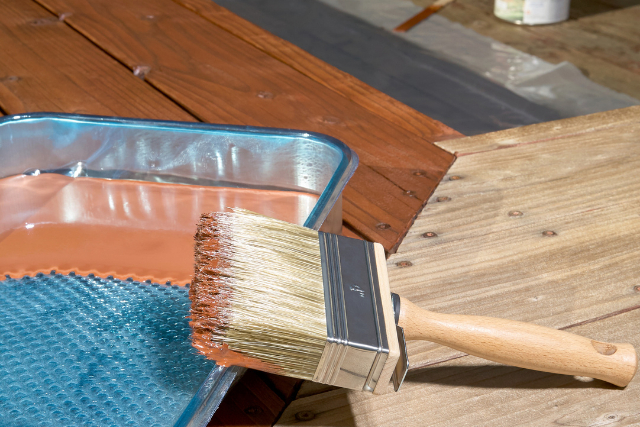 Painting a deck with a paint tray and brown paint and paint brush