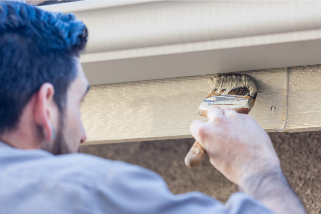 Professional exterior painter using brush to paint side of a wall.