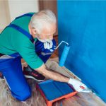 Worker wall painting a wall blue with roller and paint tray